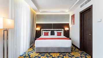 Habitación de hotel con una cama grande, cabecero, lámparas de noche, una puerta y alfombra estampada.