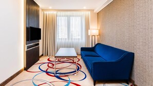 Une chambre d’hôtel avec un téléviseur à écran plat fixé sur un panneau en bois, un canapé bleu, une petite table et un lampadaire.
