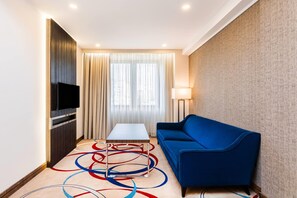 Une chambre d’hôtel avec un téléviseur à écran plat fixé sur un panneau en bois, un canapé bleu, une petite table et un lampadaire.