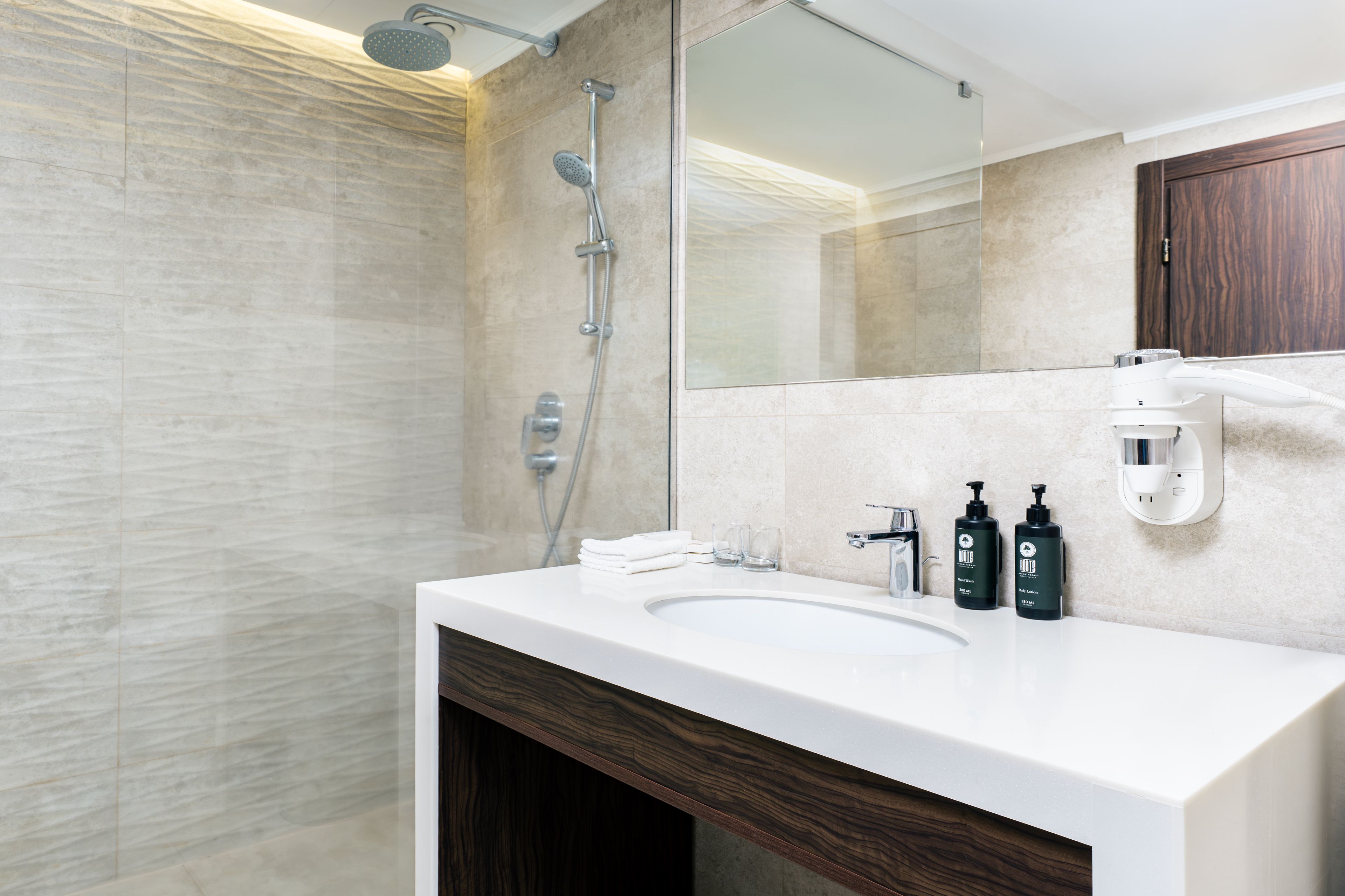 Un baño moderno con un espejo grande, ducha, lavabo y artículos de aseo.