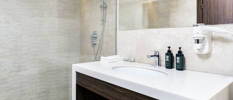 Un baño moderno con un espejo grande, ducha, lavabo y artículos de aseo.