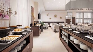Een moderne hotel eetruimte met buffettafels, een zithoek en een groot raam met gordijnen.