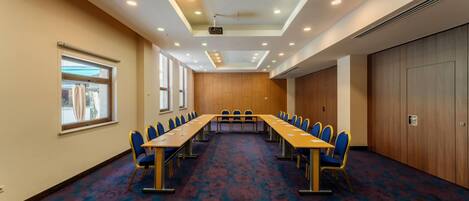A conference room with a long table and chairs, large windows, and a patterned carpet.