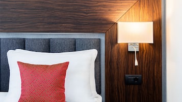 A hotel room with a bed, a red patterned pillow, a grey headboard, and a wall-mounted lamp.