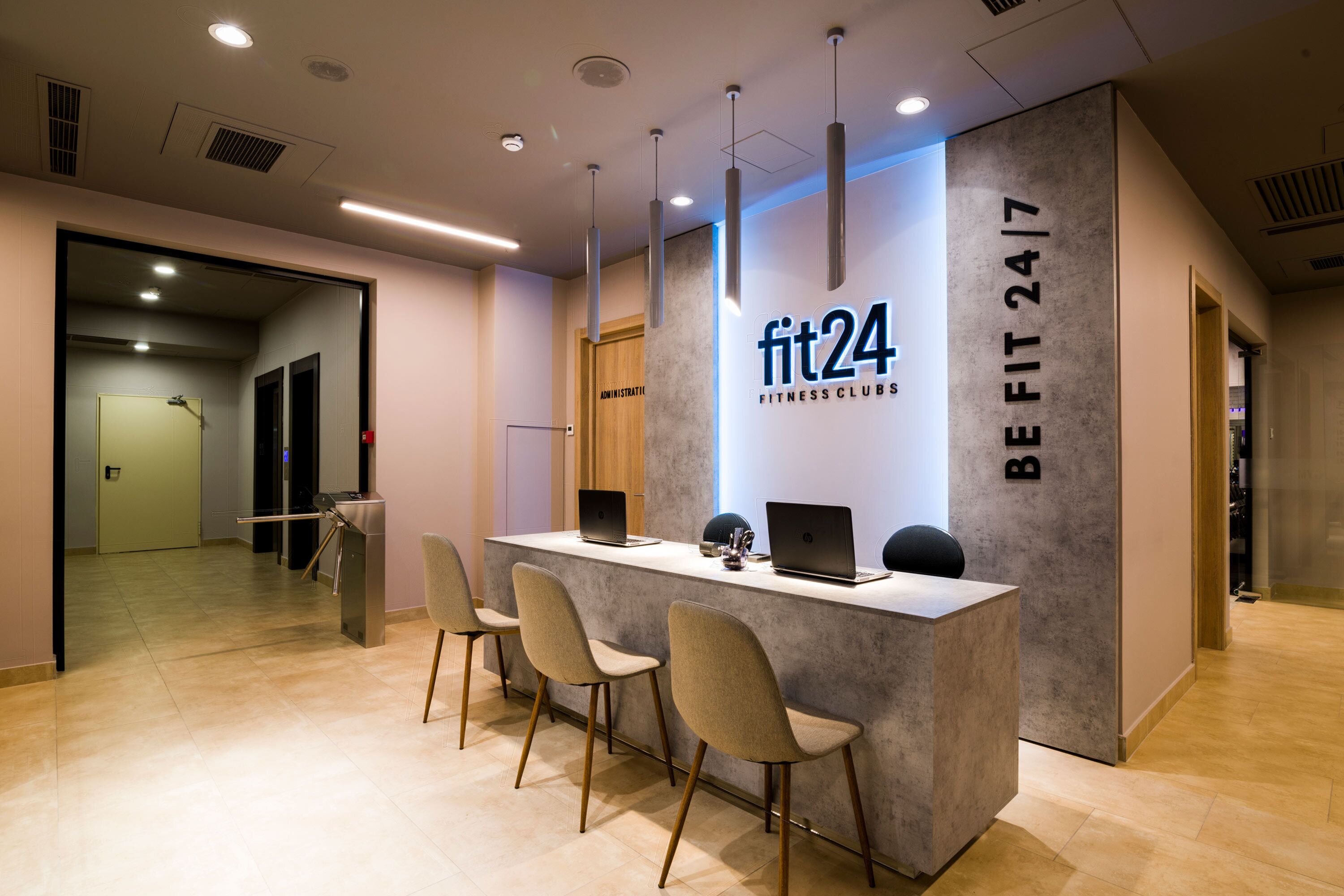 Un mostrador de recepción con un cartel que dice "fit24 FITNESS CLUBS" y "BE FIT 24/7".
