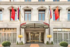 A hotel entrance with a large archway, flags, and signage for 'Ramada by Wyndham'.