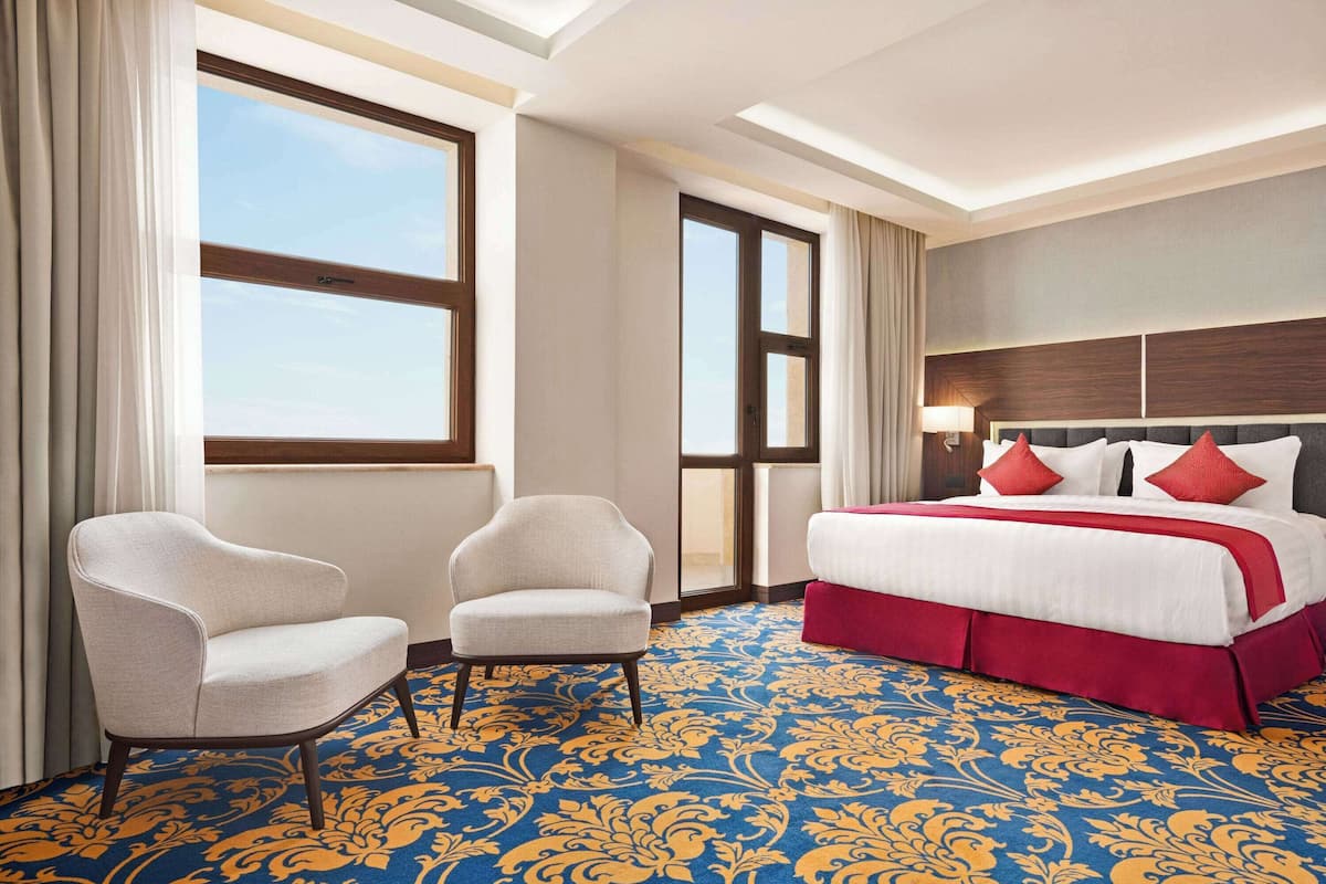 Une chambre d’hôtel avec un grand lit, deux fauteuils et une moquette à motifs.