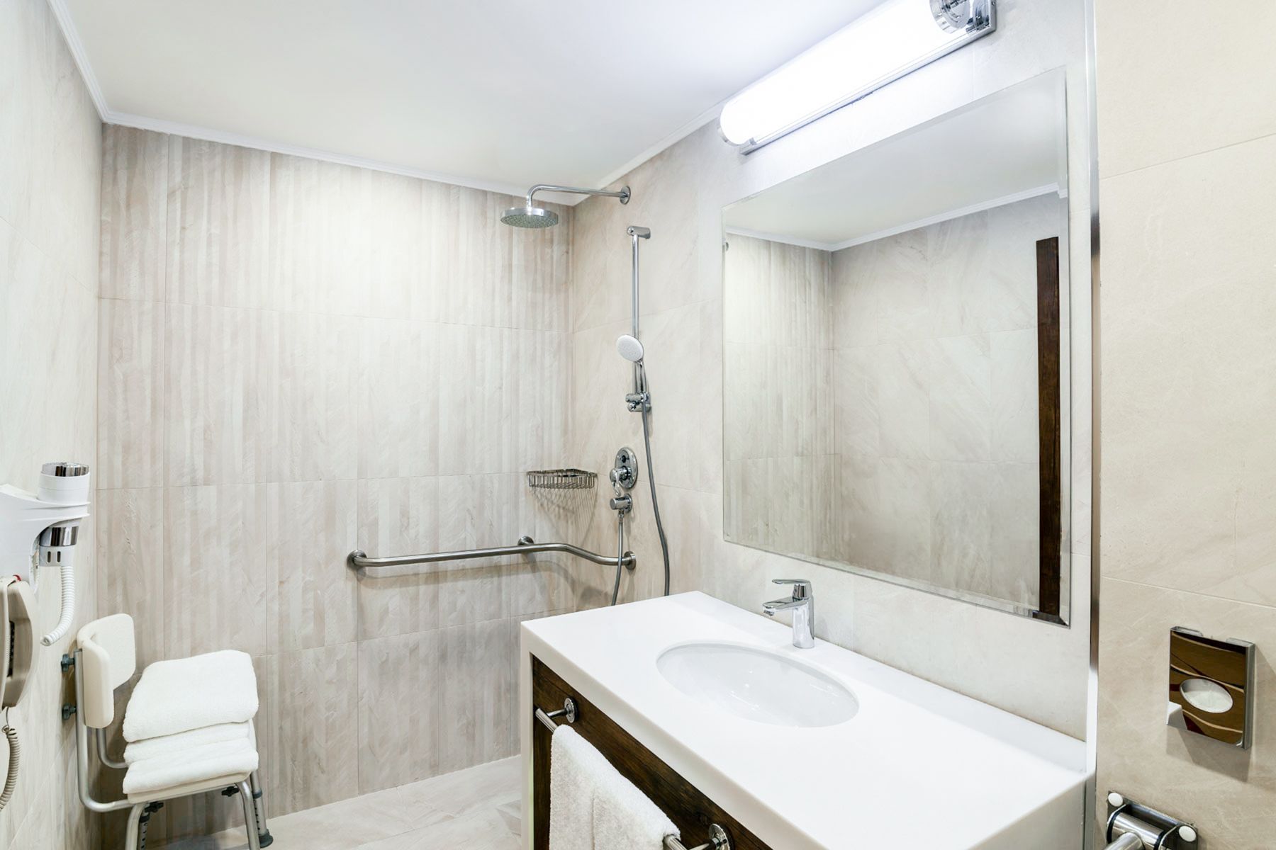 A modern bathroom with a shower, a sink, a mirror, and a wheelchair-accessible bench.