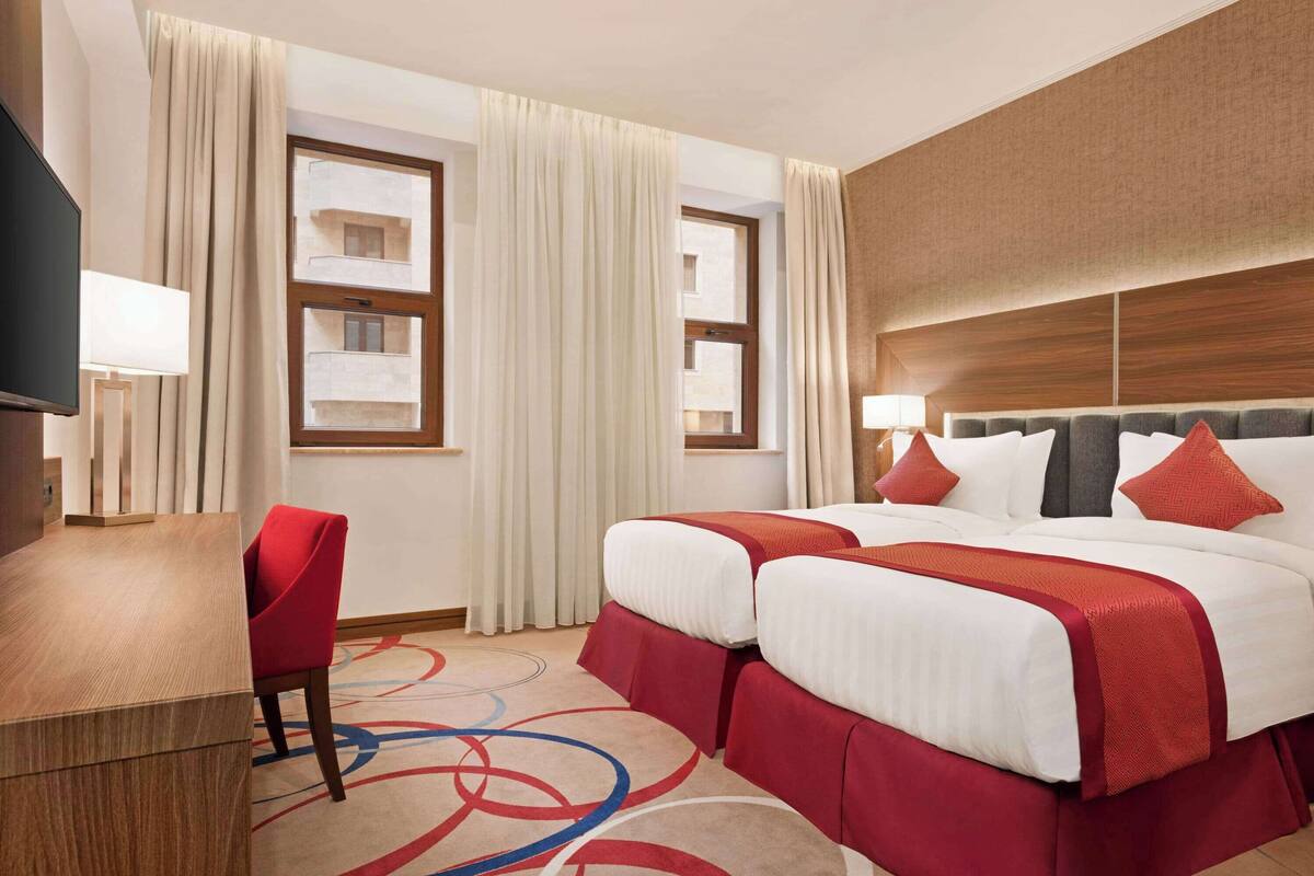 Une chambre d’hôtel avec un lit, deux fenêtres, un bureau, une chaise et un téléviseur.