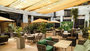 Un espace de détente intérieur aménagé avec des tables et des chaises, dont certaines sont dotées de parasols, ainsi que des plantes en pot.