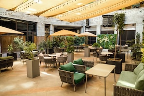 Un espace de détente intérieur aménagé avec des tables et des chaises, dont certaines sont dotées de parasols, ainsi que des plantes en pot.