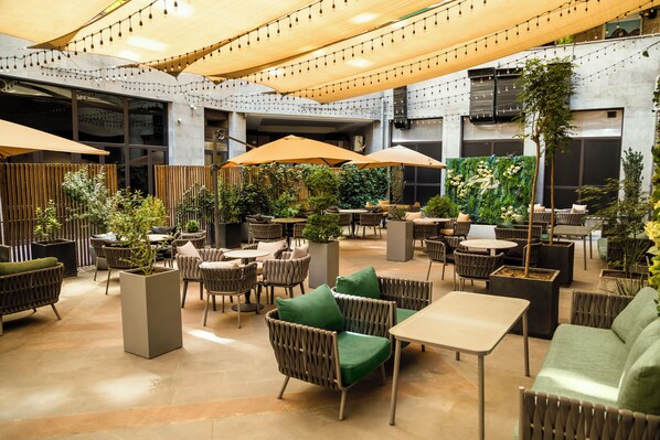 An indoor seating area with tables and chairs, some with umbrellas, and potted plants.
