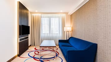 A hotel room with a flat-screen TV, a blue sofa, a small table, and a floor lamp.