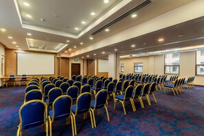 A conference room with rows of chairs, a projector screen, and an exit door.