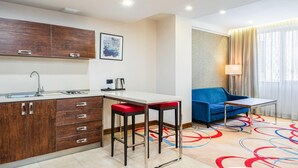 Une petite cuisine moderne équipée d’un évier, d’une cuisinière et de meubles en bois. On y trouve une petite table avec une chaise rouge, un canapé bleu et une lampe près d’une fenêtre ornée de rideaux.