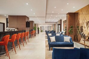 Eine moderne Hotelhalle mit Barbereich, Sitzgelegenheiten und einem großen Bildschirm.