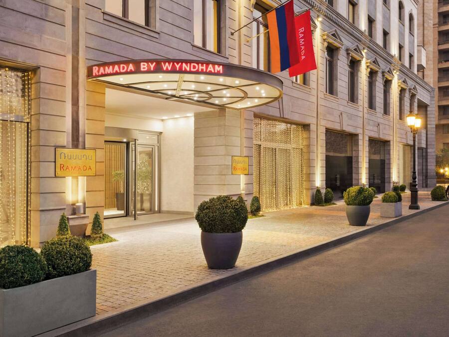 Entrada de um hotel com uma placa indicando "Ramada by Wyndham" e uma bandeira.