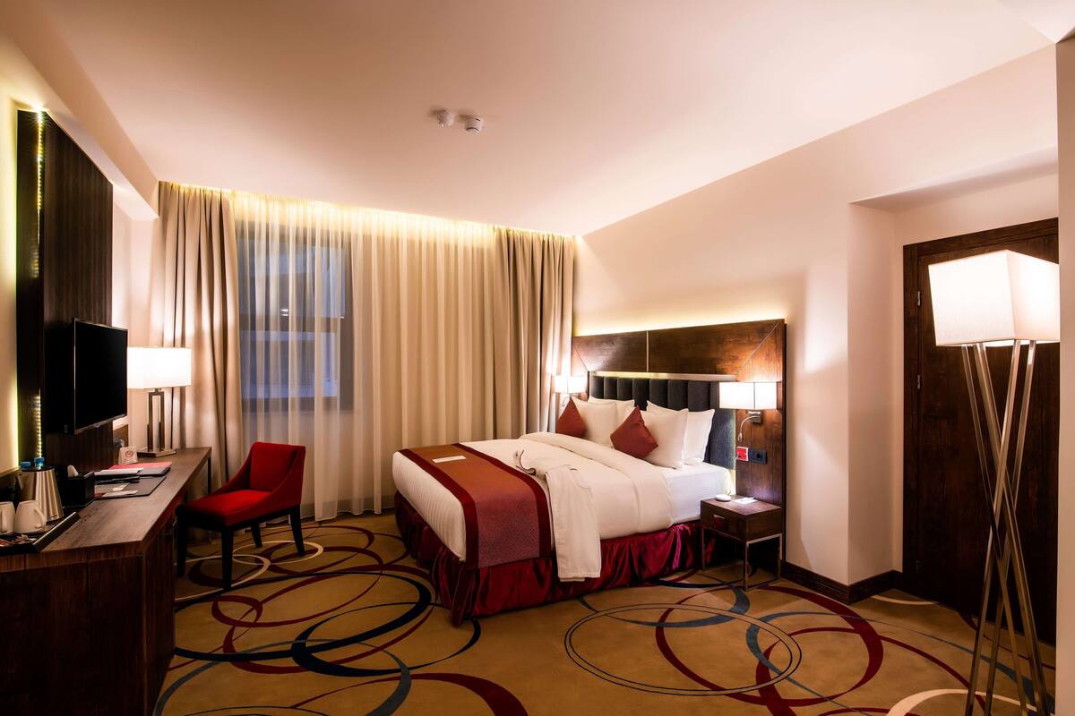 Une chambre d’hôtel comprenant un lit, un bureau avec une chaise, une télévision et une fenêtre avec des rideaux.