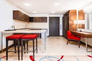 Een moderne keuken met een centraal eiland, barkrukken en een eethoek met een rode stoel.