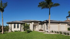 A two-story house with a flat roof, a front lawn, and a driveway. - Gulf access home, private pool, Jacuzzi, great waterview, free WIFI (Cape Coral,)