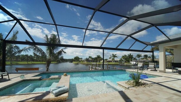 A pool area with a glass enclosure, a hot tub, and a view of a lake and palm trees. - Gulf access home, private pool, Jacuzzi, great waterview, free WIFI (Cape Coral,)