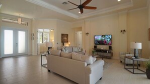 A spacious living room with a beige sofa, a ceiling fan, a flat-screen TV, and a dining area with a table and chairs. - Gulf access home, private pool, Jacuzzi, great waterview, free WIFI (Cape Coral,)
