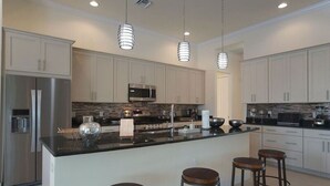 A modern kitchen with white cabinets, stainless steel appliances, a central island with stools, and pendant lighting. - Gulf access home, private pool, Jacuzzi, great waterview, free WIFI (Cape Coral,)