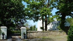 A gated entrance with a stone wall and potted plants, leading to a white building with multiple windows. - Hartley House B&B (Carrick-on-Shannon)