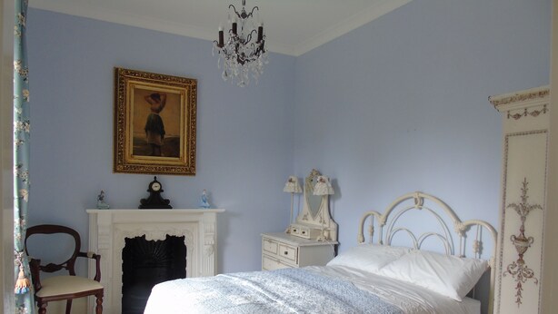 A bedroom with a bed, a dresser, a chair, a fireplace, and a chandelier. - Hartley House B&B (Carrick-on-Shannon)
