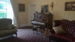 A room with a grand piano, a red sofa, a patterned carpet, and a chandelier. - Hartley House B&B (Carrick-on-Shannon)