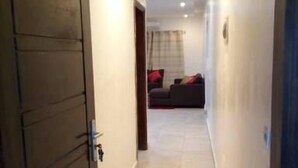A hallway with a wooden door on the left, a tiled floor, and a dark-colored sofa in the background. - Residence djoumah (Abidjan)