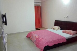 A single-bed room with a pink bedspread, a dark headboard, and a red curtain partially visible in the background. - Residence djoumah (Abidjan)