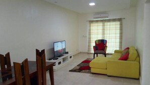 A living room with a yellow sofa, a TV on a stand, a dining table with chairs, and a colorful chair. - Residence djoumah (Abidjan)