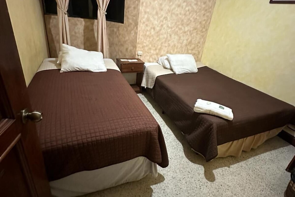 Ein Hotelzimmer mit zwei Betten, einem Nachttisch, einem Fenster mit Vorhängen und einer Wand mit Struktur.