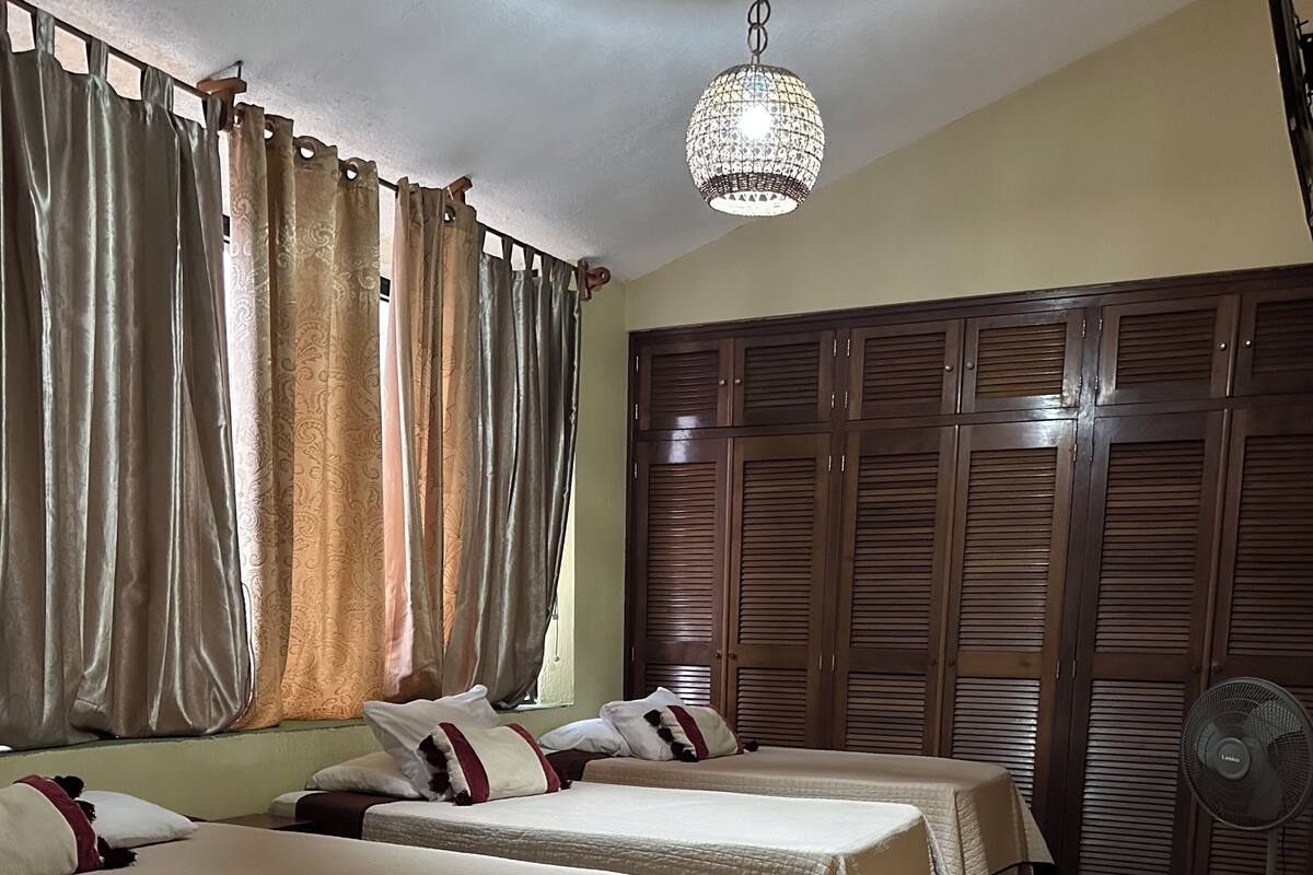 Ein Hotelzimmer mit zwei Betten, einem großen Kleiderschrank, einer Deckenleuchte und einem Standventilator.