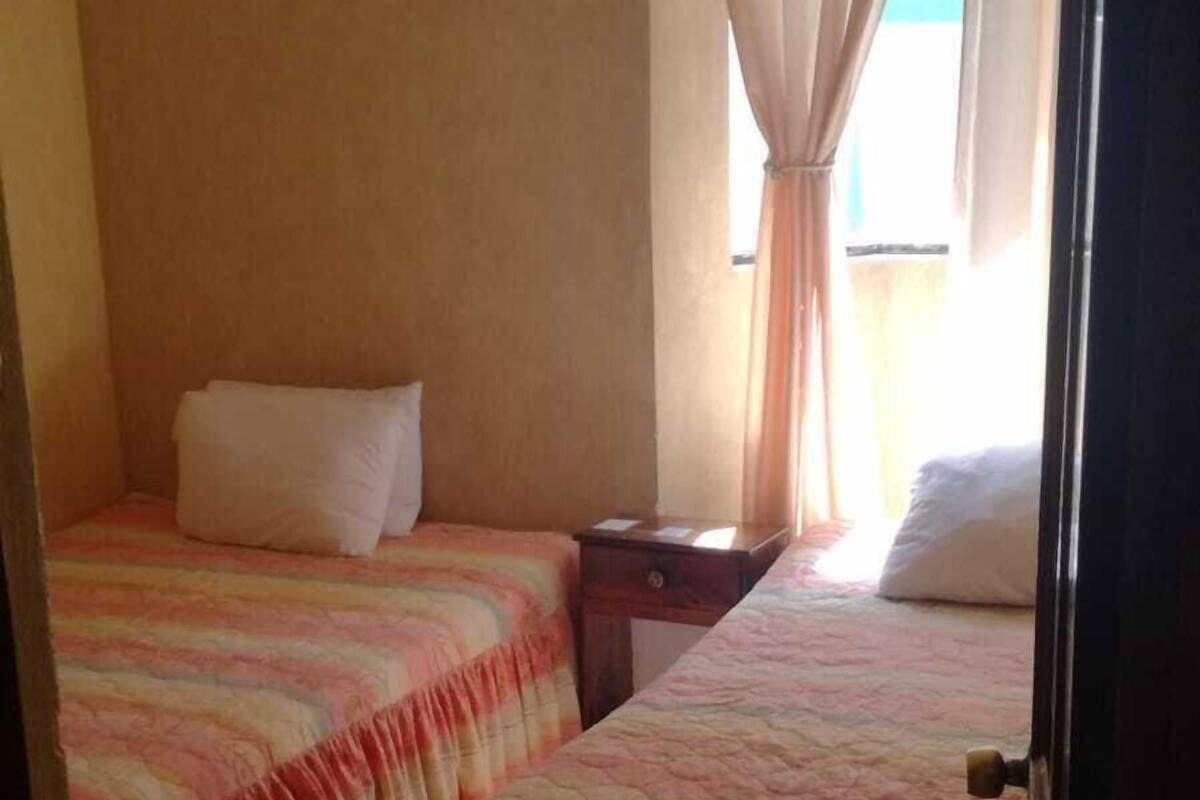 Ein Hotelzimmer mit zwei Betten, einem kleinen Tisch und einem Fenster mit Vorhängen.