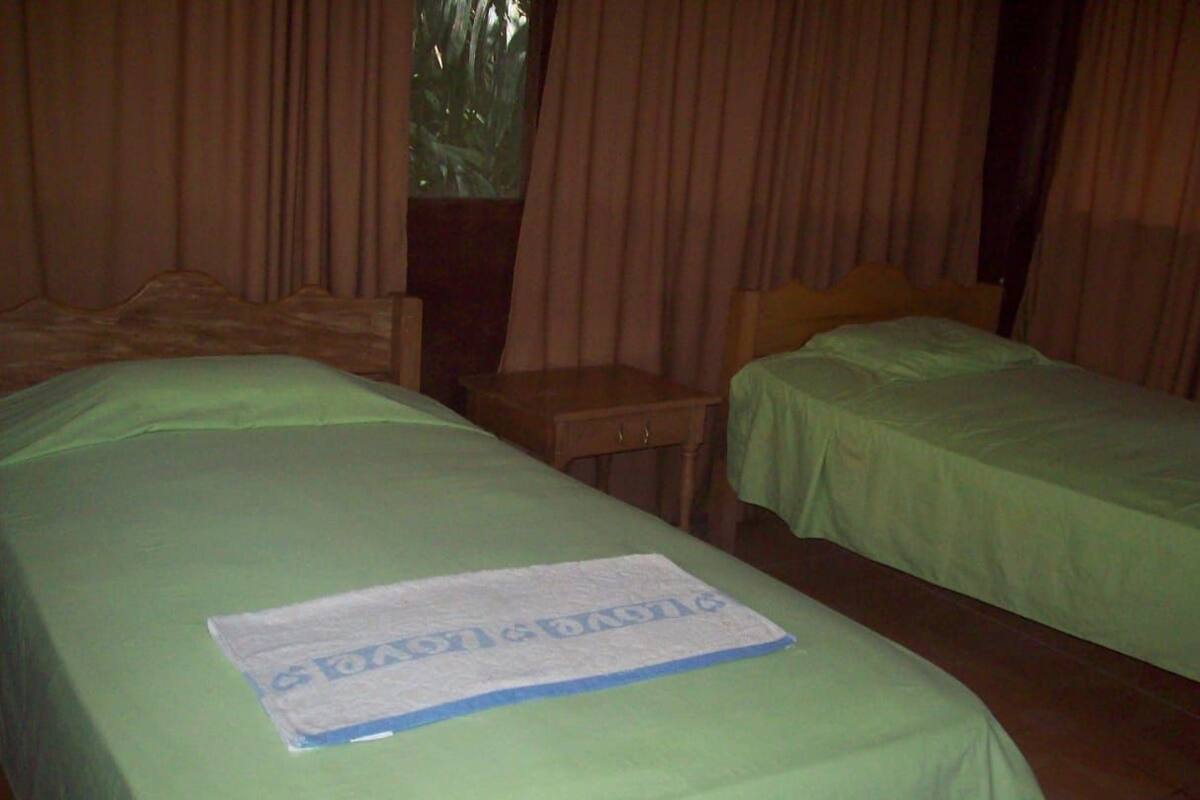 A hotel room with two beds, a wooden nightstand, and a window with curtains.