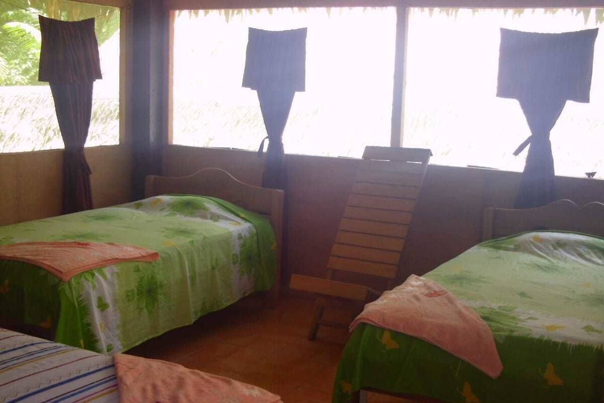 A room with two single beds, a wooden chair, and a window with curtains.