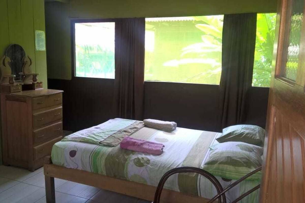 A bedroom with a bed, a wooden dresser, and a window with curtains.