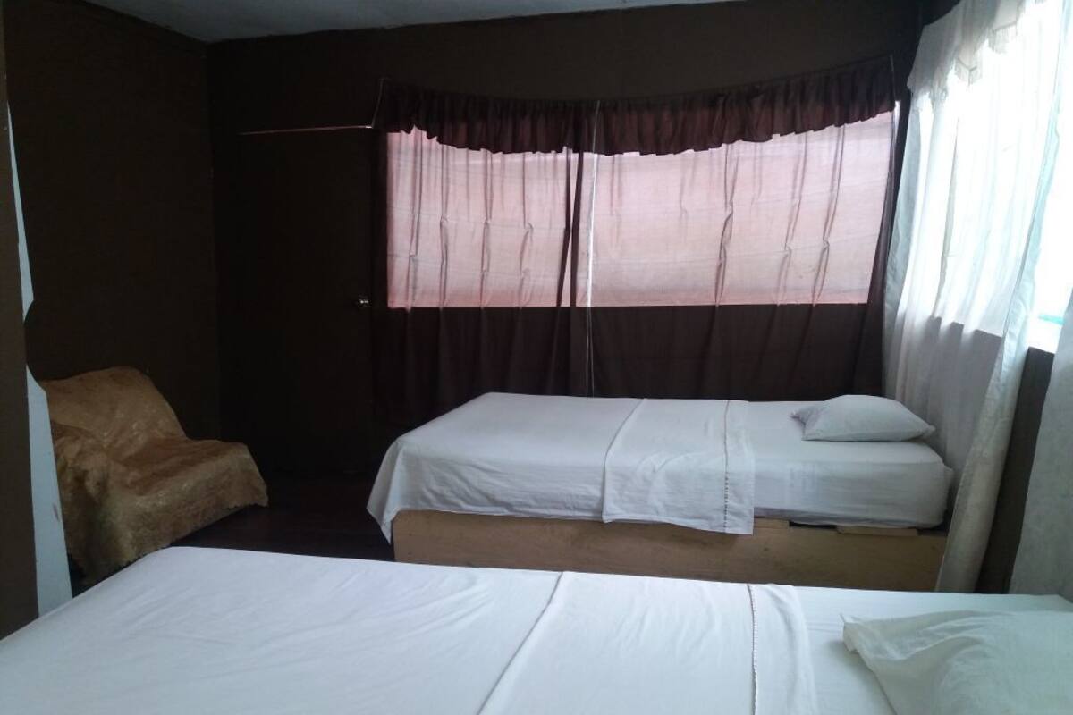 A room with two beds, a chair, and a window with curtains.