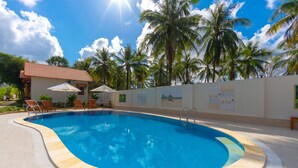 A swimming pool with a tiled edge, surrounded by lounge chairs and umbrellas, with palm trees and a building in the background. - Phu Quoc Bungalow Yen Thanh (Phu Quoc)
