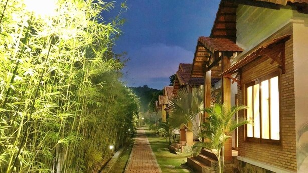 A pathway lined with bamboo and palm trees leading to a row of brick buildings with wooden roofs. - Phu Quoc Bungalow Yen Thanh (Phu Quoc)