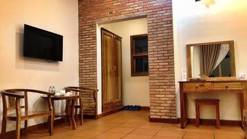 A room with a brick wall, a television mounted on the wall, a wooden desk with a mirror, and a wooden chair.