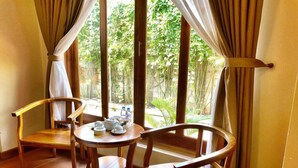 A room with two wooden chairs, a small round table with teapots and cups, and a view of greenery through large windows. - Phu Quoc Bungalow Yen Thanh (Phu Quoc)
