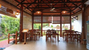An indoor dining area with wooden tables and chairs, a ceiling fan, and large windows offering a view of greenery outside. - Phu Quoc Bungalow Yen Thanh (Phu Quoc)