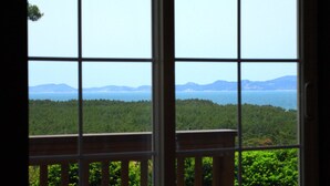 A view through a window with a balcony, overlooking a forested area and distant mountains. - Petit Maison Pension (Taean)