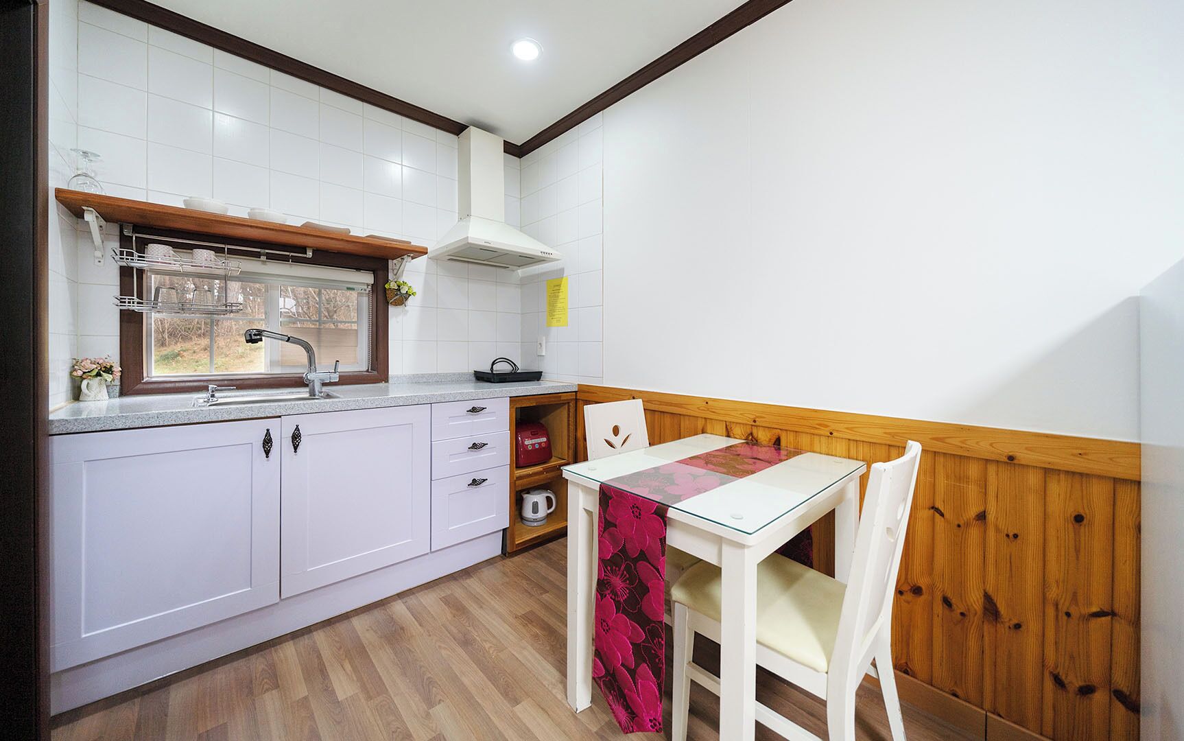 A compact kitchen with white cabinets, a wooden countertop, a window above the sink, and a table with chairs.