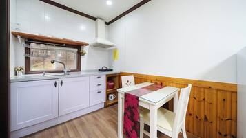 A compact kitchen with white cabinets, a wooden countertop, a window above the sink, and a table with chairs.