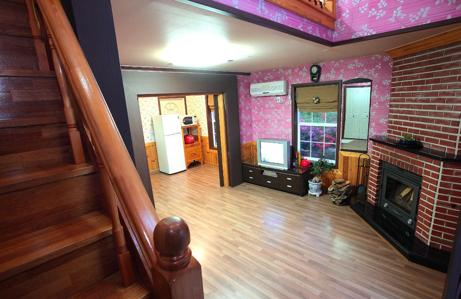 A spacious living area with a wooden staircase, a fireplace, and a kitchen area in the background.