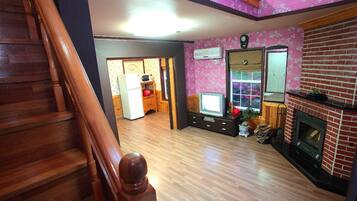 A spacious living area with a wooden staircase, a fireplace, and a kitchen area in the background.